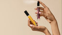 Two small bottles of perfume held by a hand against a beige background